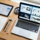 Open Design AI. A designer's workspace with a laptop displaying website designs, a tablet with wireframes, and a notebook of sketches